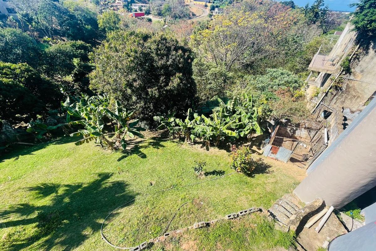 An elevated aerial view of the property's rear garden area, featuring sloped terrain, mature trees, and a fenced outdoor enclosure.