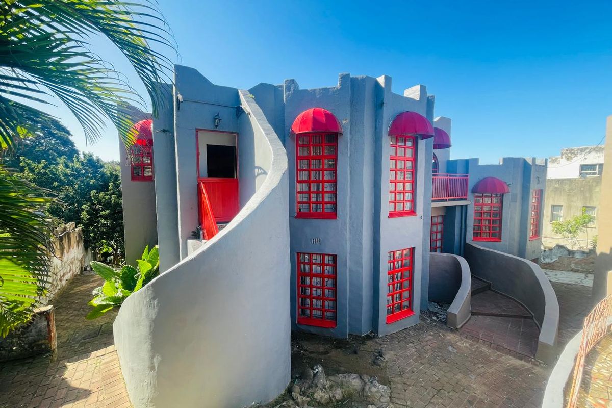 Rear exterior view of a unique multi-level home featuring a prominent curved staircase, red window frames, and matching red fabric awnings.