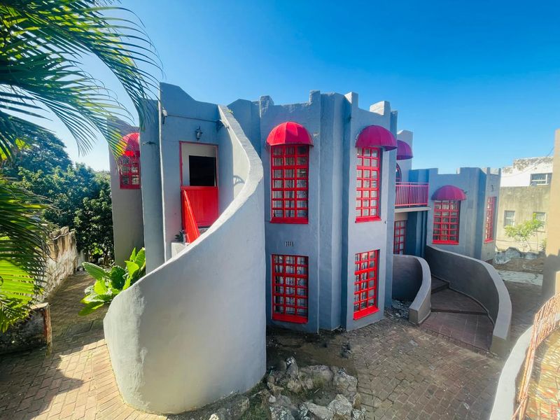 Rear exterior view of a unique multi-level home featuring a prominent curved staircase, red window frames, and matching red fabric awnings.