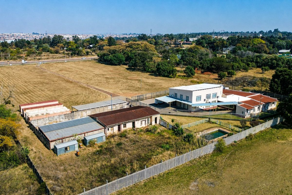 Aerial view of a residential property featuring multiple outbuildings, a swimming pool, and extensive surrounding land with perimeter fencing.