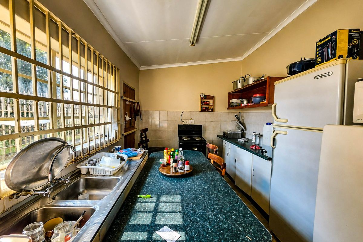 A functional kitchen featuring a double stainless steel sink, laminate countertops, tiled backsplash, and built-in cabinetry with security bars on the window.