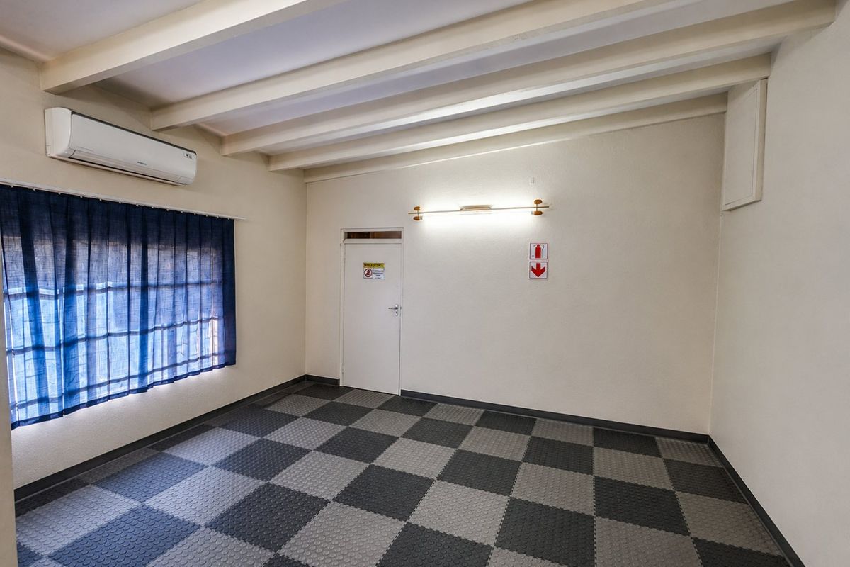 A clean, vacant room featuring exposed ceiling beams, a split-system air conditioner, and durable interlocking floor tiles, suitable for various residential uses.
