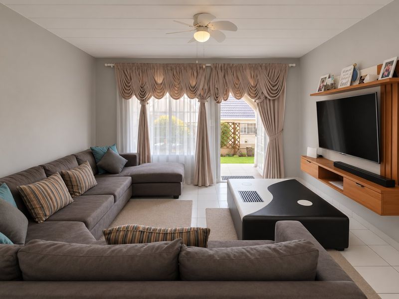 A well-maintained living room featuring tiled flooring, a ceiling fan, and a built-in media console, with direct access to an outdoor patio area.