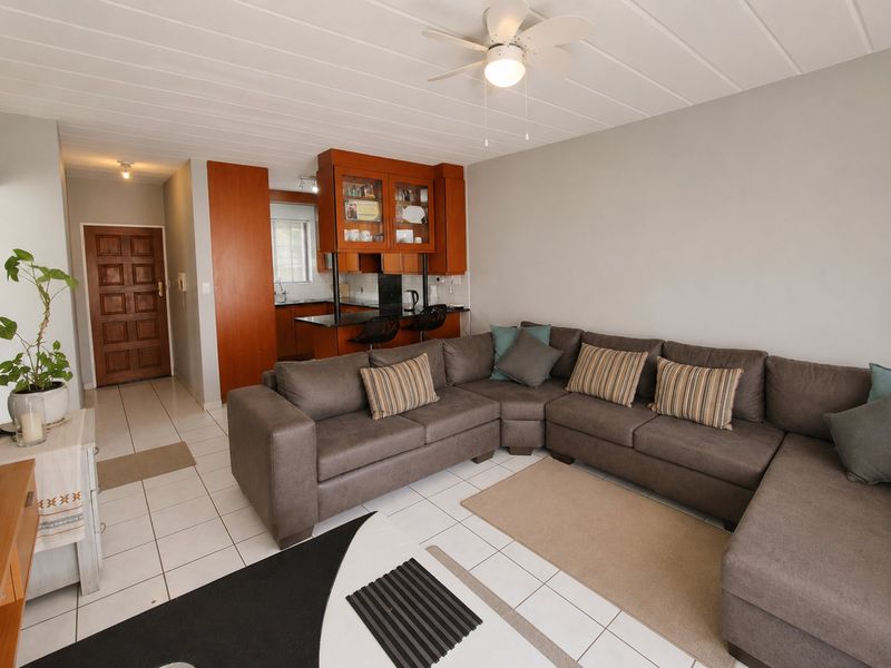 Open-plan living area featuring tiled flooring, a ceiling fan, and a functional kitchen with built-in cabinetry and a breakfast bar.