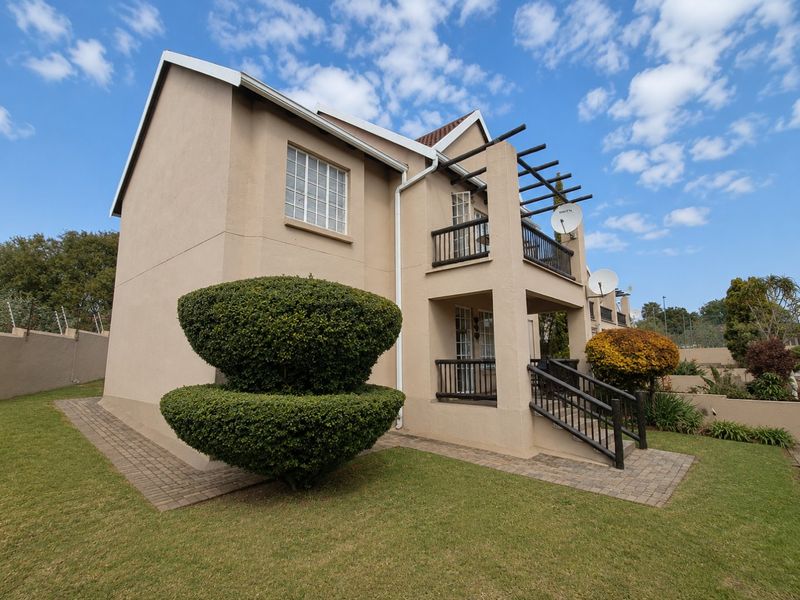 Rear view of the apartment building featuring a ground floor patio, upper level balcony with pergola, and paved access paths set within a landscaped garden.