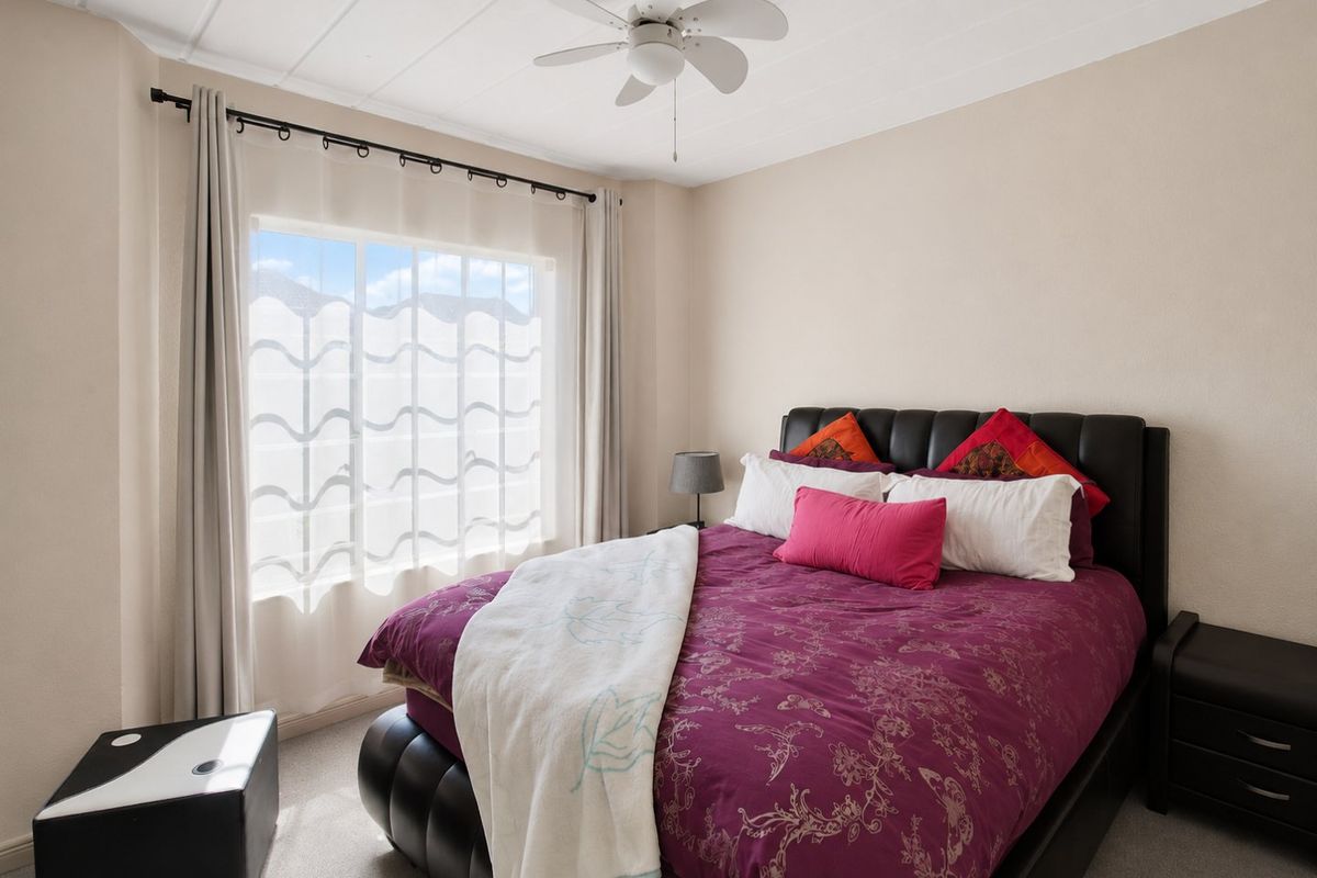 A well-maintained bedroom featuring neutral wall tones, carpeted flooring, and a functional ceiling fan, providing a comfortable and inviting living space.