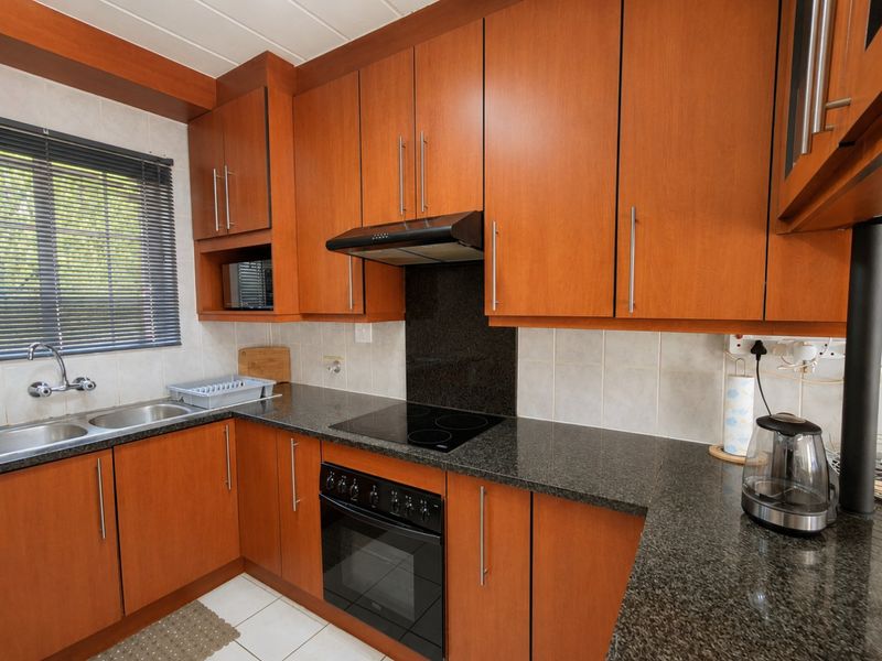 A functional kitchen featuring warm-toned wooden cabinetry, granite countertops, a built-in oven with an electric hob, and a tiled backsplash.