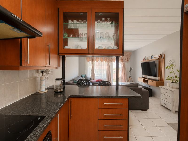 Open-plan kitchen featuring wooden cabinetry, granite countertops, and an electric hob, flowing seamlessly into the adjacent living area with tiled flooring throughout.