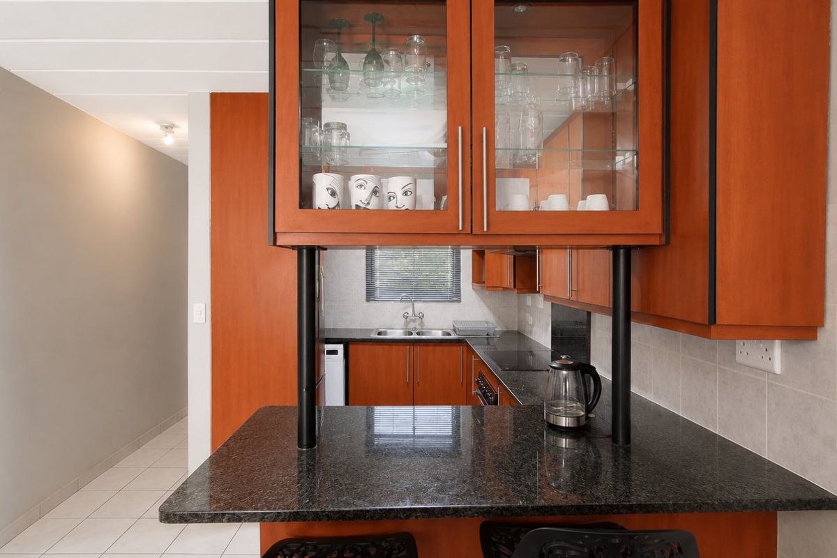 A functional kitchen featuring warm-toned wooden cabinetry, granite countertops, a double sink, and a breakfast bar area with glass-fronted display storage.