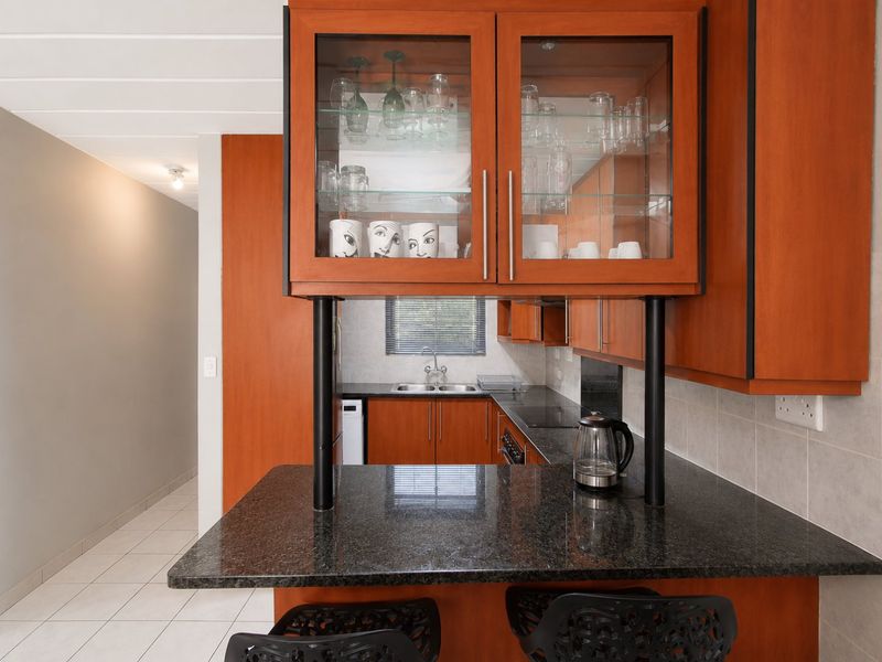 A functional kitchen featuring warm-toned wooden cabinetry, granite countertops, a double sink, and a breakfast bar area with glass-fronted display storage.