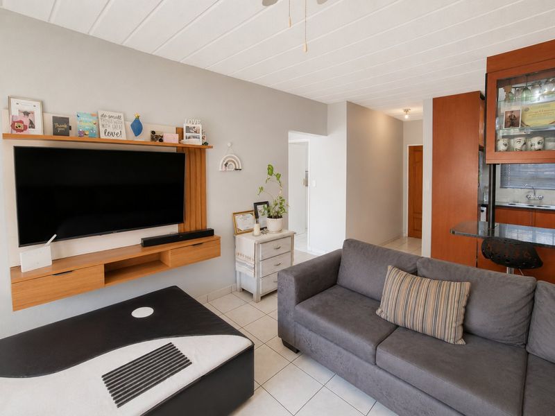 Open plan living area featuring tiled floors, a built-in media console, and an adjacent kitchen with breakfast bar and wooden cabinetry.