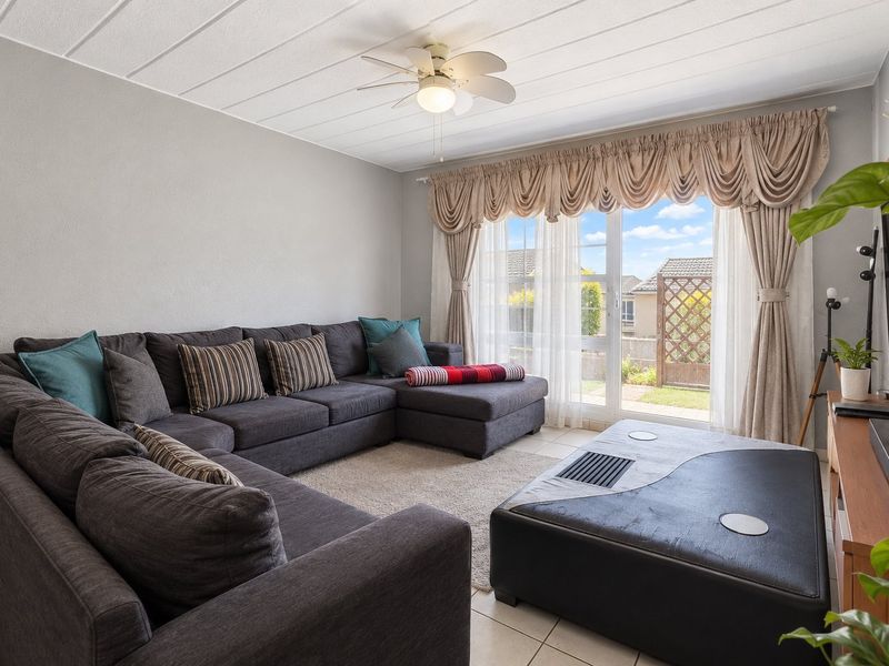 A comfortable living room featuring tiled flooring, a ceiling fan, and a sliding glass door providing access to the outdoor area.