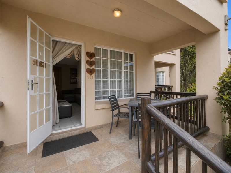 A covered patio area featuring tiled flooring, a timber railing, and direct access to the interior through a white-framed french door.