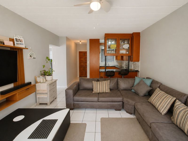 Open plan living area featuring tiled flooring, a timber panelled ceiling, and a functional kitchen with built-in cabinetry and a breakfast bar.