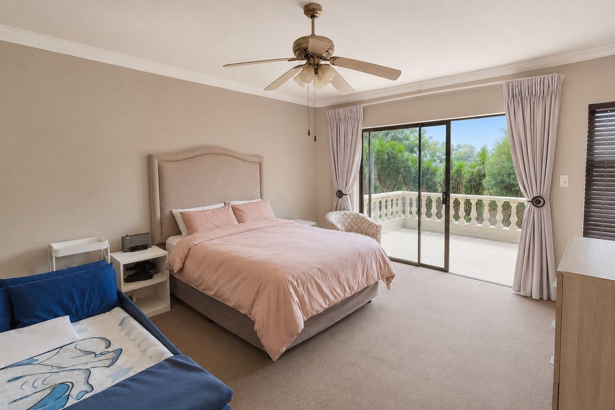 Spacious bedroom featuring neutral carpeting, a ceiling fan, and large sliding glass doors opening onto a private balcony with balustrade detailing.