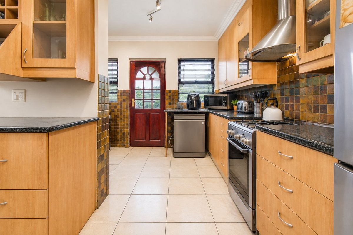 A functional kitchen featuring light wood cabinetry, granite countertops, a stainless steel gas stove with extractor fan, and tiled splashbacks.