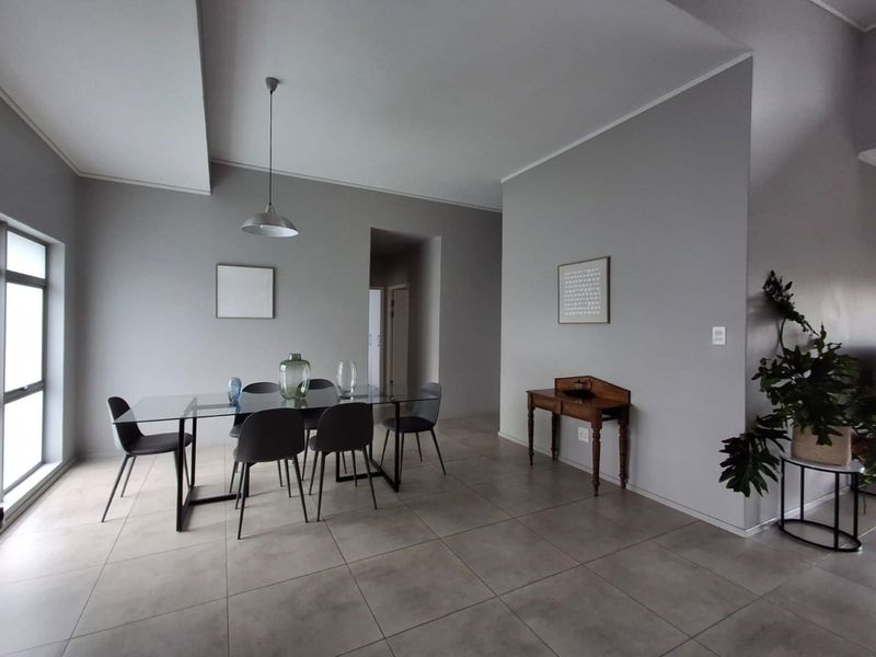 A bright and spacious dining area featuring neutral tiled flooring, modern pendant lighting, and large windows allowing for ample natural light.