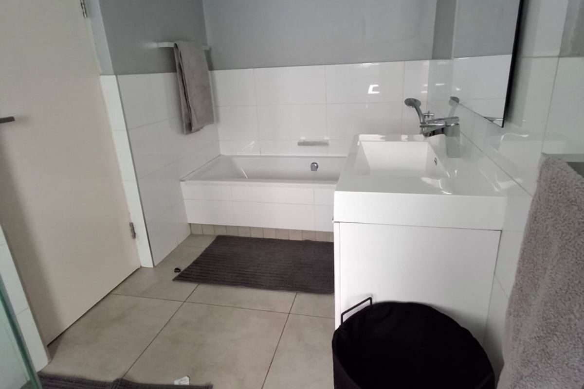 A modern, clean bathroom featuring a built-in bathtub, a sleek vanity basin with a large mirror, and neutral tiled finishes.