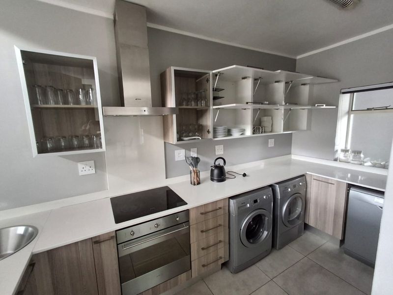 Modern kitchen featuring sleek laminate cabinetry, stone countertops, built-in oven, electric hob, extractor fan, and integrated laundry appliance space.