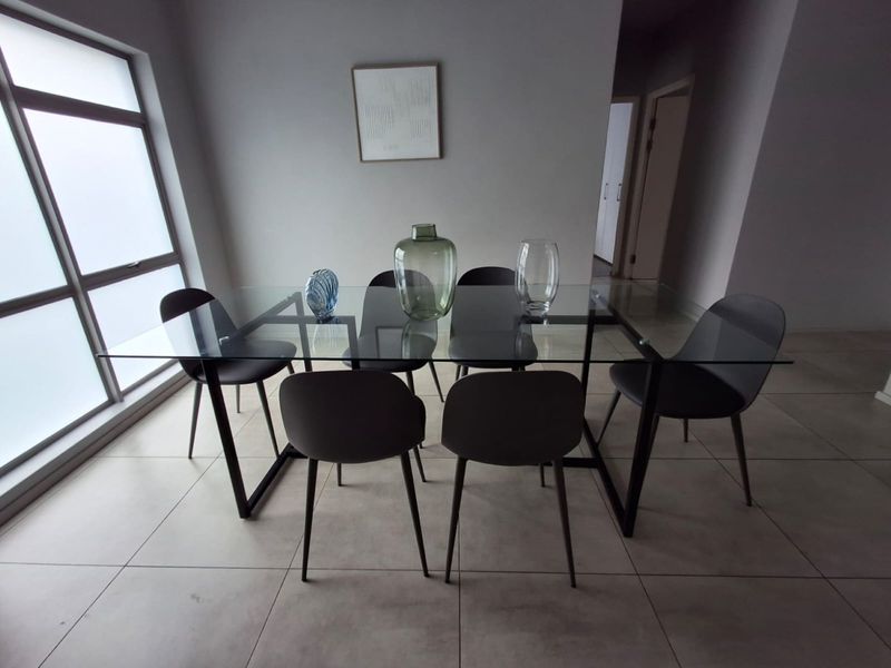 A bright dining area featuring large windows and neutral tiled flooring, providing a clean and modern space for meals.