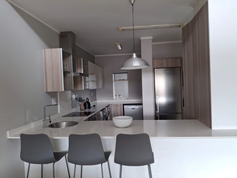 Modern kitchen featuring sleek cabinetry, stone countertops, integrated appliances, and a breakfast bar with pendant lighting, creating a functional and contemporary cooking space.