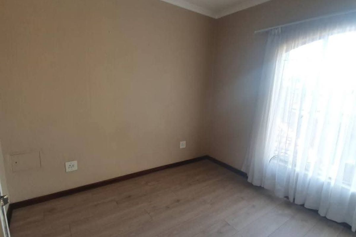 An empty bedroom featuring laminate flooring, neutral walls, and a window with sheer curtains, offering a blank canvas for personalization.