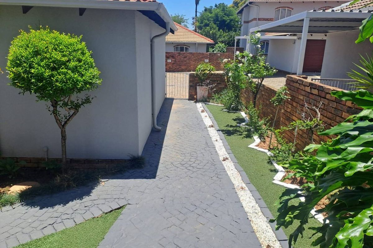 A well-maintained rear exterior area featuring a paved walkway, artificial lawn, and brick boundary wall, providing a clean and low-maintenance outdoor space.