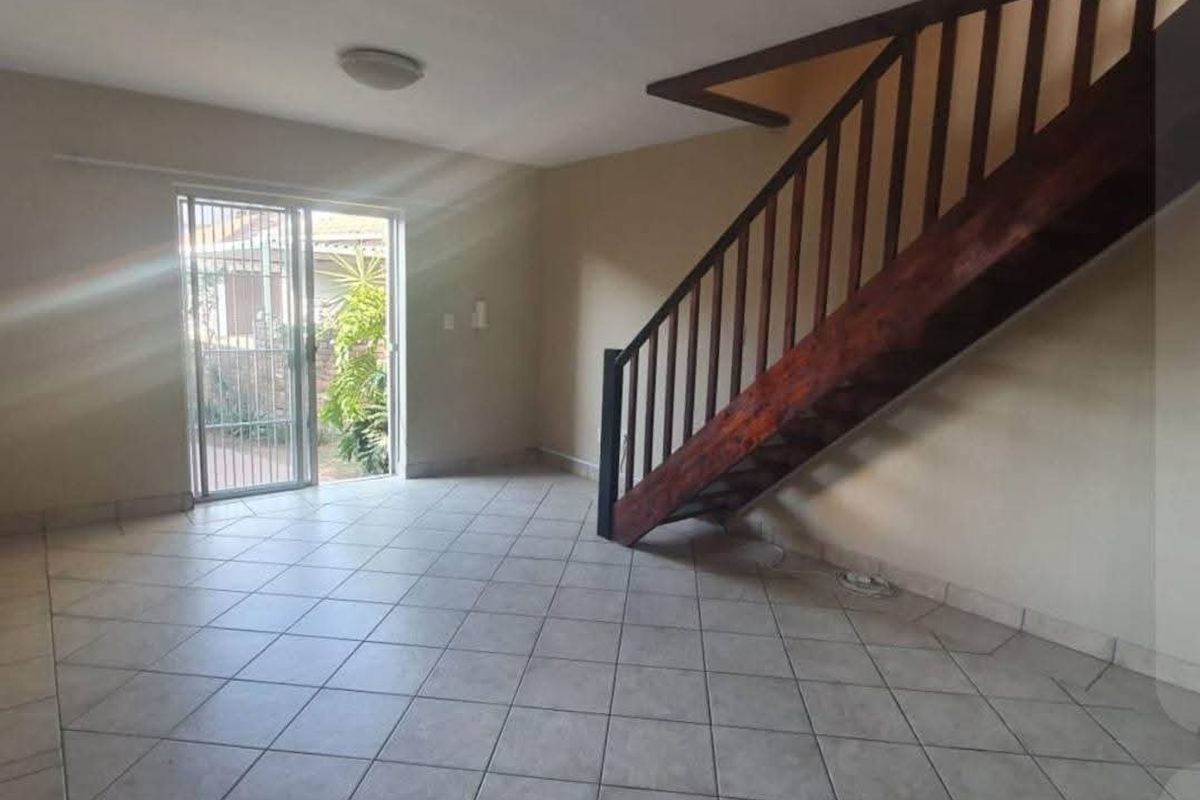 An open-plan living area featuring tiled flooring and a wooden staircase, with direct access to the exterior through a sliding glass door.