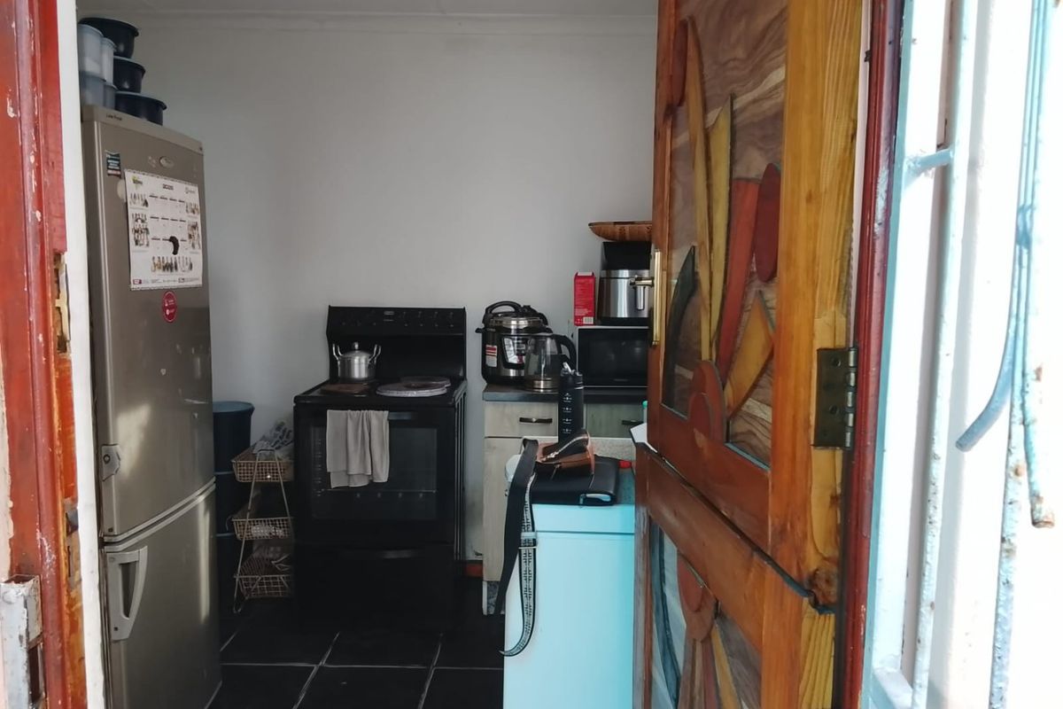 A compact kitchen area featuring tiled flooring, a freestanding stove, and basic cabinetry, accessible through a decorative wooden door.