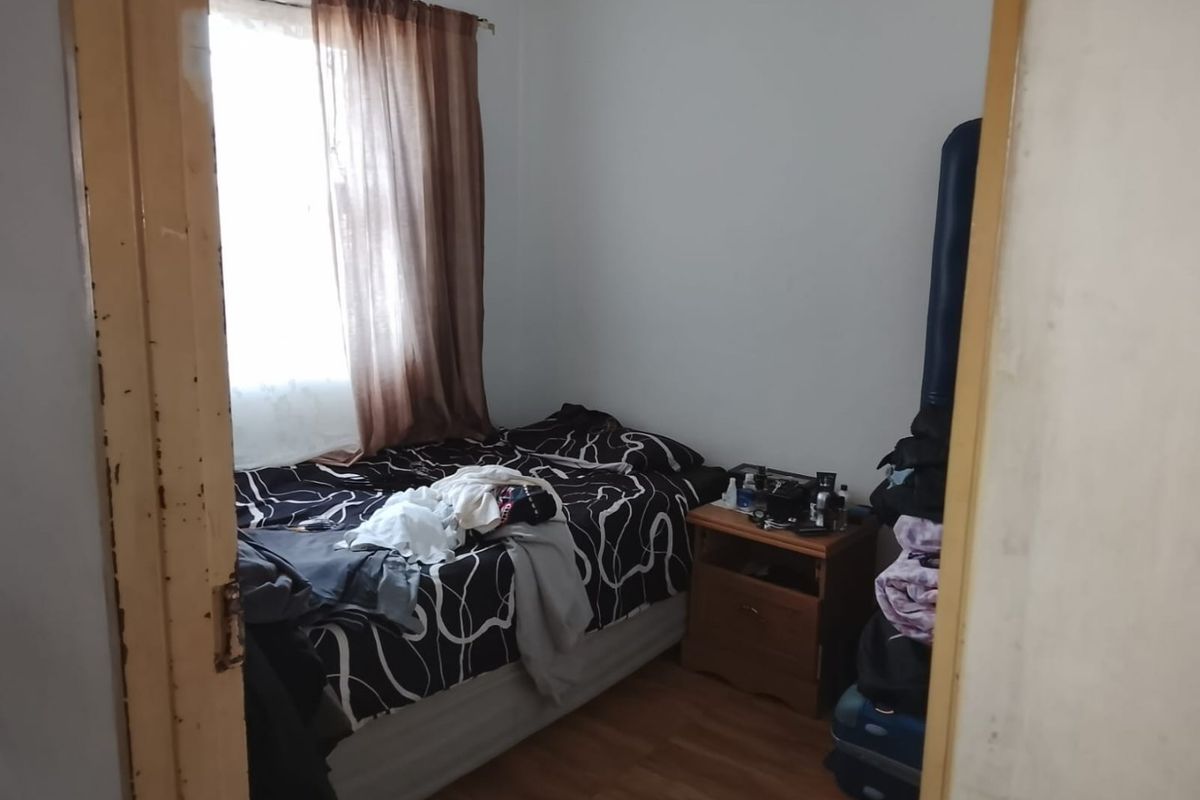 A compact bedroom featuring laminate flooring and a window, currently showing signs of wear on the door frame.