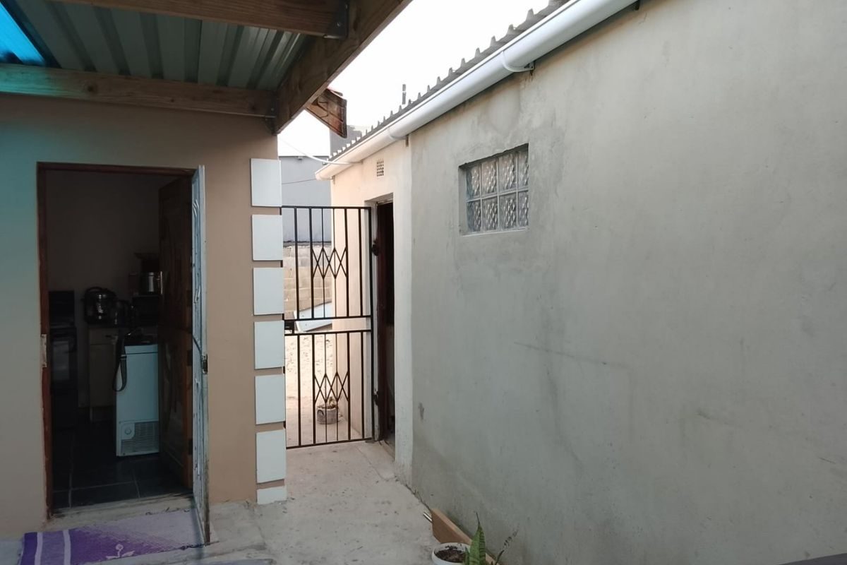 A rear exterior view showing a covered patio area, security gate, and access to the interior, featuring basic finishes and functional outdoor space.