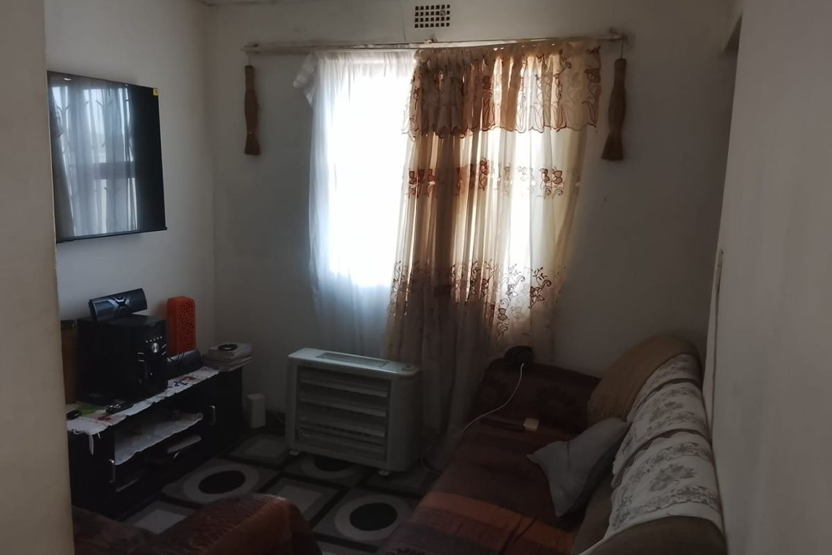 A compact living room featuring a ventilation brick and standard window placement, currently requiring cosmetic updates to improve the overall aesthetic.