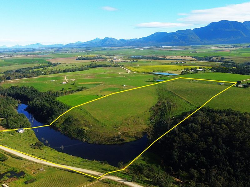 Aerial view of a large farm property featuring expansive green pastures, river frontage, and scenic mountain views in the background.