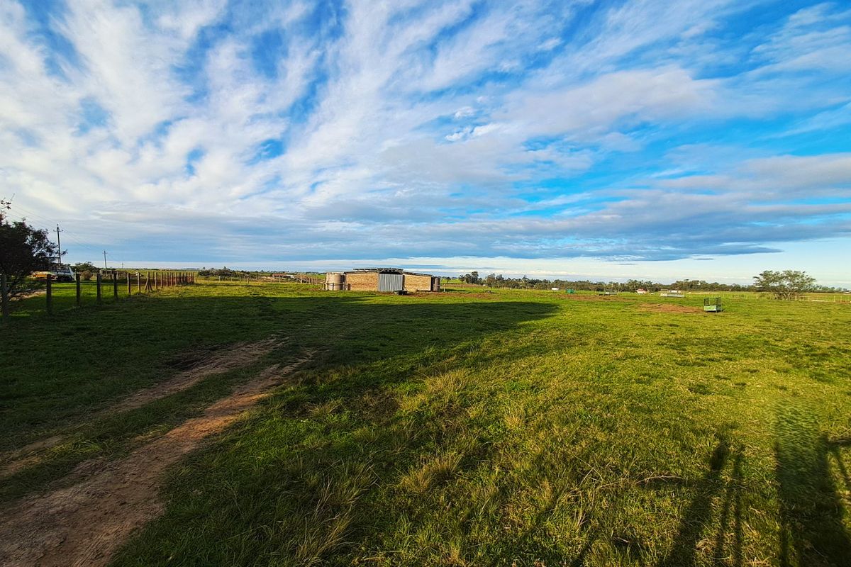 A wide-angle view of the farm property featuring open grazing land, wire fencing, and a distant outbuilding with water storage tanks.