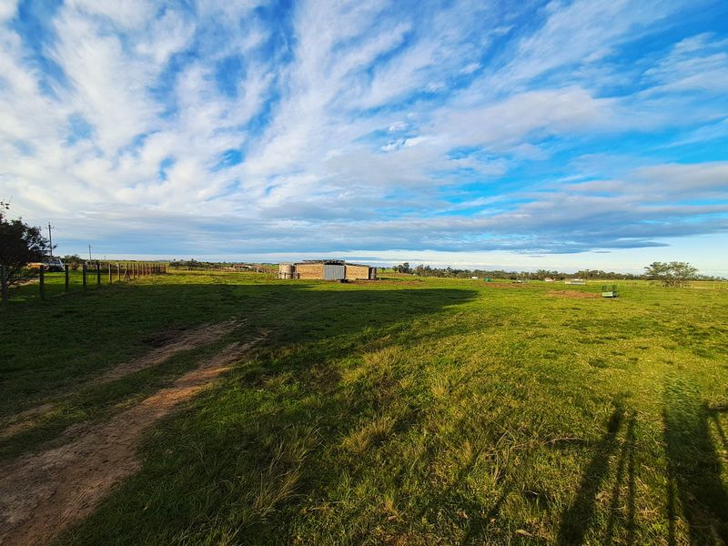 A wide-angle view of the farm property featuring open grazing land, wire fencing, and a distant outbuilding with water storage tanks.