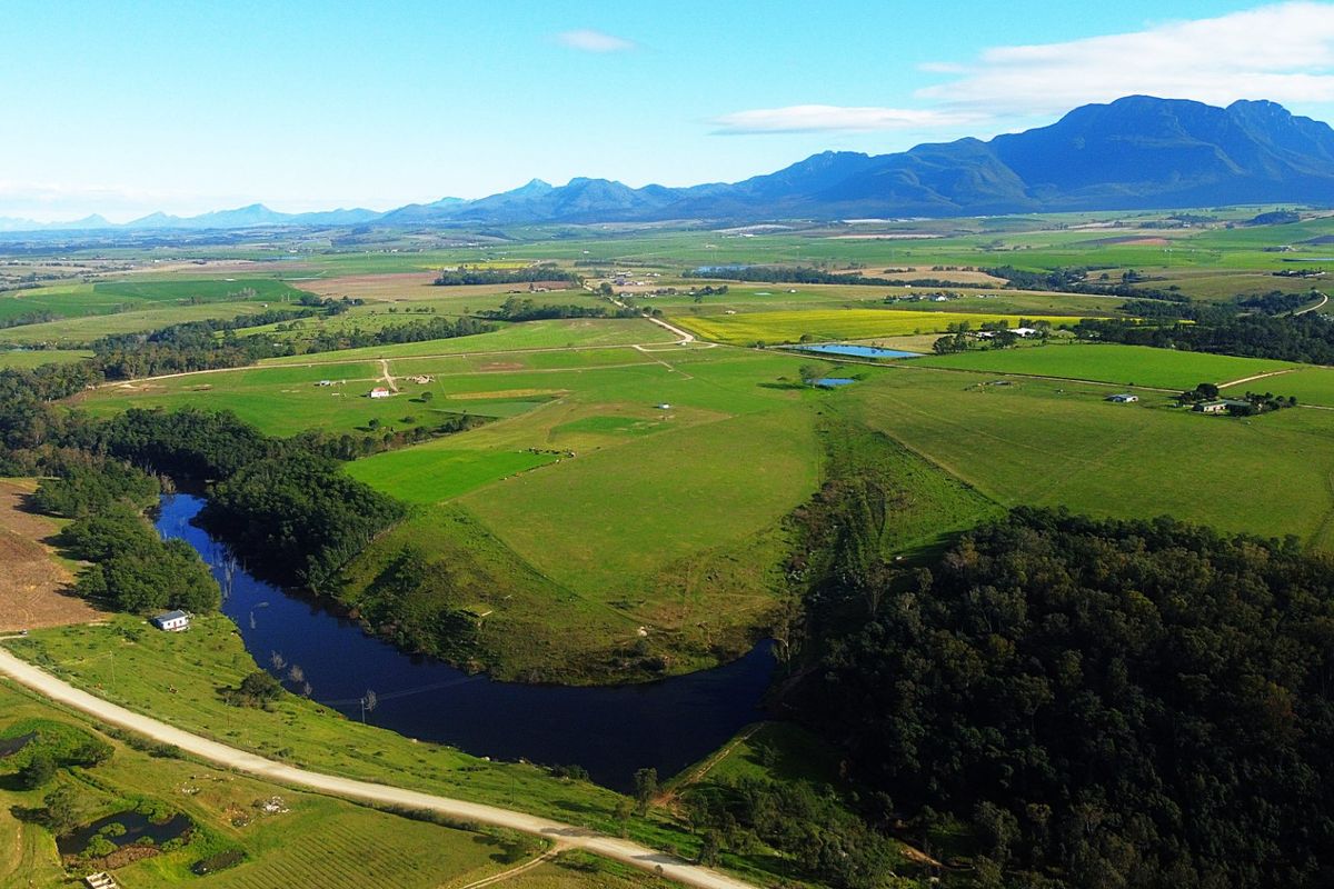 An expansive aerial view of the farm property featuring lush green pastures, a winding river, and scenic mountain views in the distance.