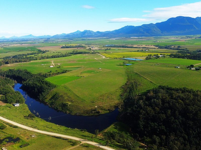 An expansive aerial view of the farm property featuring lush green pastures, a winding river, and scenic mountain views in the distance.
