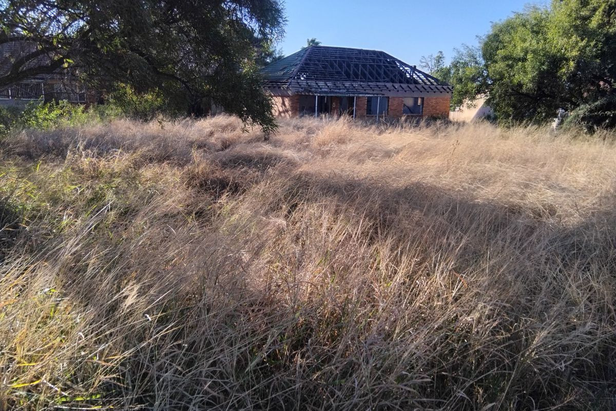 A view of a residential property lot featuring an existing brick structure with missing roof covering, surrounded by overgrown dry grass.