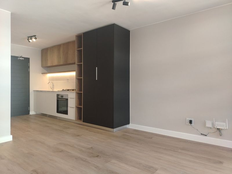 Modern open-plan living area featuring a sleek kitchen with built-in cabinetry, integrated oven, hob, and contemporary wood-look laminate flooring.