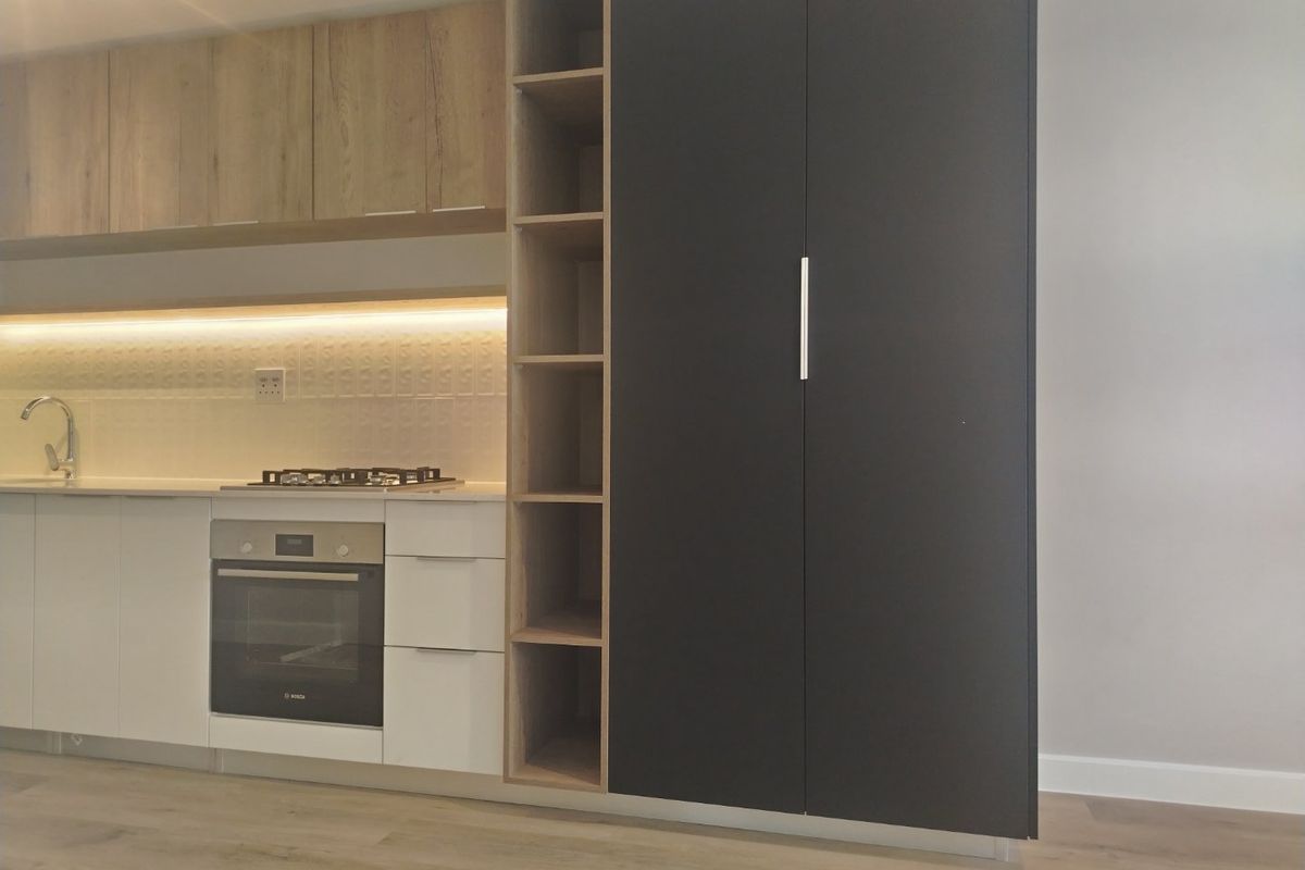 Modern kitchen featuring sleek white and dark cabinetry, built-in oven, gas hob, and integrated shelving with warm under-cabinet lighting.