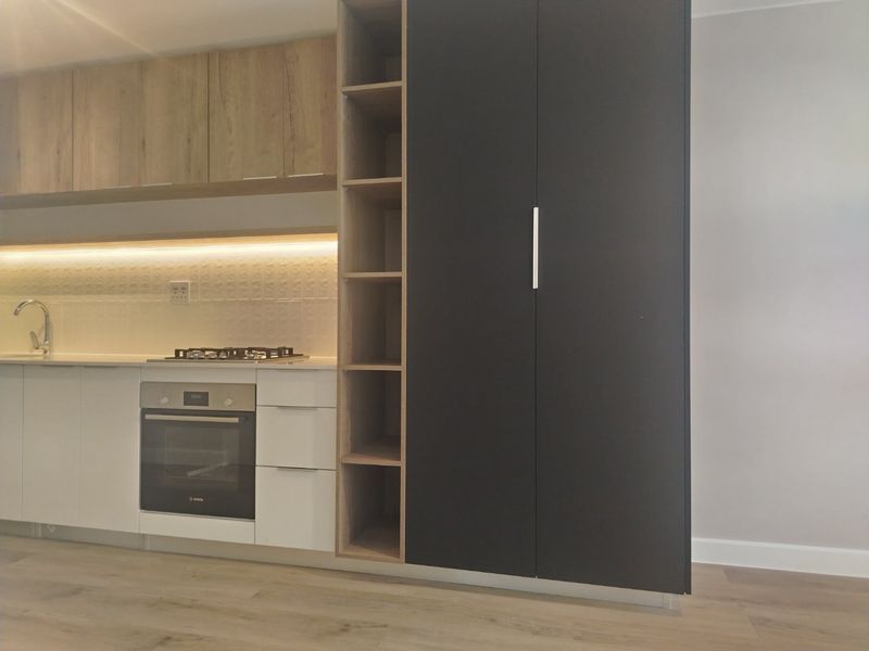 Modern kitchen featuring sleek white and dark cabinetry, built-in oven, gas hob, and integrated shelving with warm under-cabinet lighting.