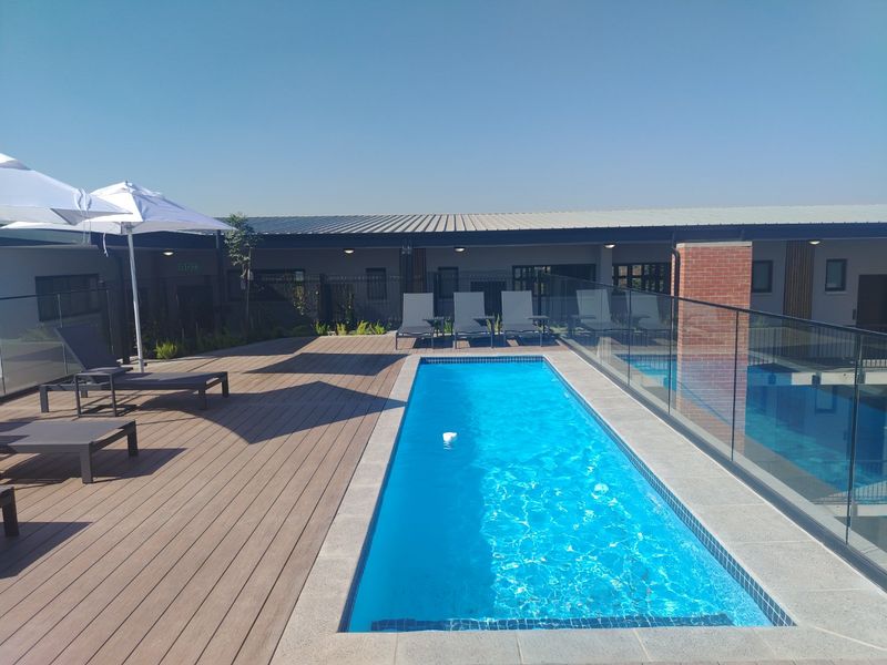 A well-maintained outdoor pool area featuring modern timber decking, a clear glass balustrade, and a clean swimming pool.