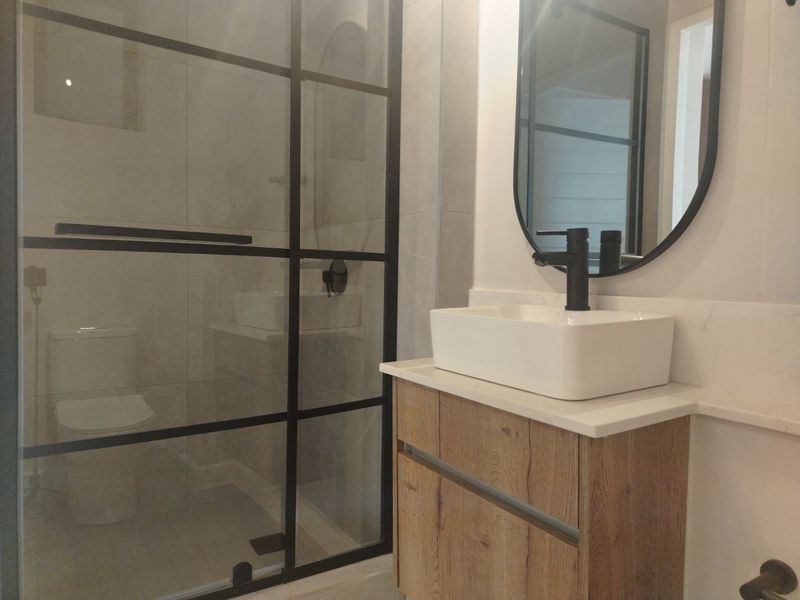 Modern bathroom featuring a vessel sink on a wood-finish vanity, black fixtures, and a contemporary black-framed glass shower enclosure.