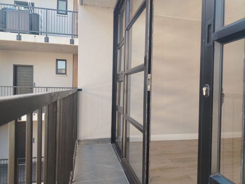 A modern apartment balcony featuring dark metal balustrades and a large sliding glass door providing access to the interior living space.