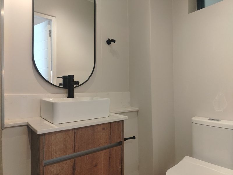 Modern bathroom featuring a wood-finish vanity with a vessel sink, stone countertop, black fixtures, and a sleek wall-mounted mirror.