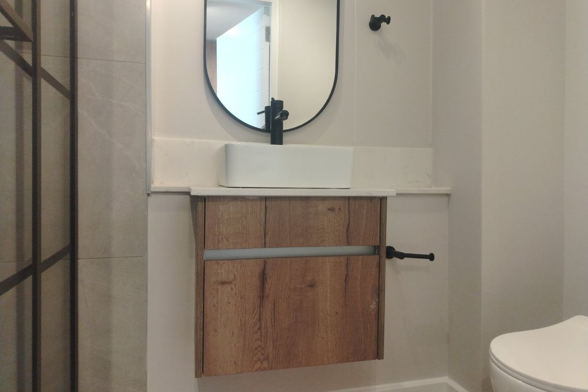 Modern bathroom featuring a wall-mounted wood-finish vanity, vessel sink with black fixtures, stone countertop, and a sleek black-framed mirror.