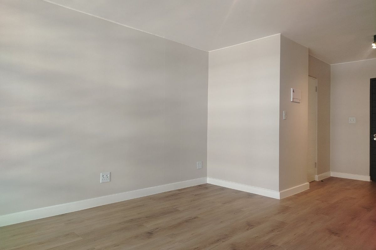 A bright, empty living area featuring modern laminate flooring, neutral walls, and clean finishes, ready for personalization.