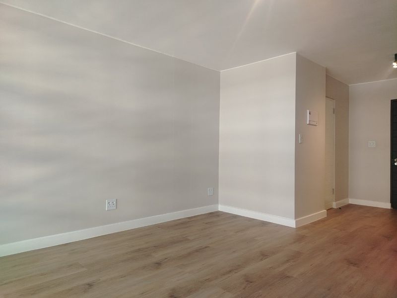 A bright, empty living area featuring modern laminate flooring, neutral walls, and clean finishes, ready for personalization.