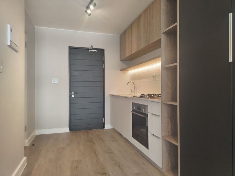 Modern compact kitchen featuring sleek cabinetry, integrated oven, gas hob, and warm under-cabinet lighting, finished with high-quality laminate flooring.