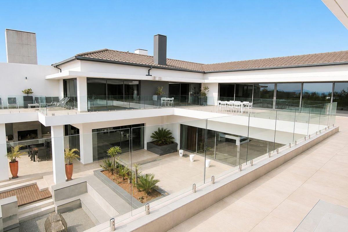 Spacious multi-level rear exterior featuring expansive tiled patios, glass balustrades, and seamless indoor-outdoor flow through large sliding glass doors.